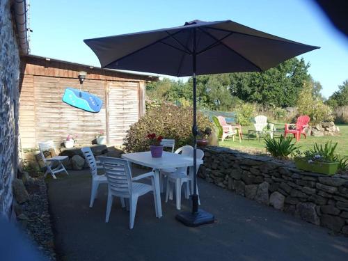 uma mesa e cadeiras com um guarda-sol num pátio em Charmante longère près des côtes Finistériennes em Plouégat-Guérand