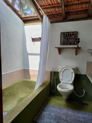 a bathroom with a toilet and a bath tub at Caju Grove - The Big Yellow Goan House in Guirim