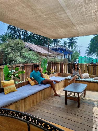 a man and a woman sitting on a wooden deck at Caju Grove - The Big Yellow Goan House in Guirim