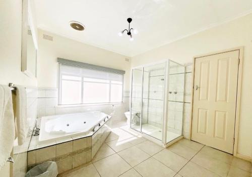 La salle de bains est pourvue d'une baignoire, d'une douche et d'une fenêtre. dans l'établissement Connells Motel & Serviced Apartments, à Traralgon