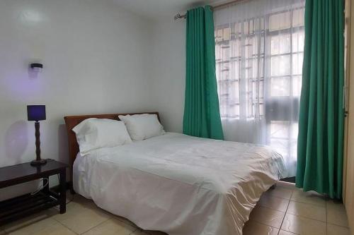 1 dormitorio con 1 cama con cortinas verdes y ventana en 2 bedroom Apt 20 min to JKIA Airport,SGR Train St., en Athi River
