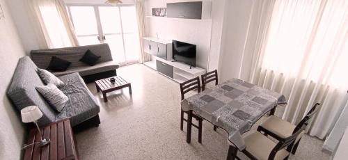uma sala de estar com um sofá e uma mesa com uma televisão em Apartamento Rincon de Loix, soleado, zona jardines y piscina, y zona exterior para aparcar y a la playa a 300,00 mts. em Benidorm