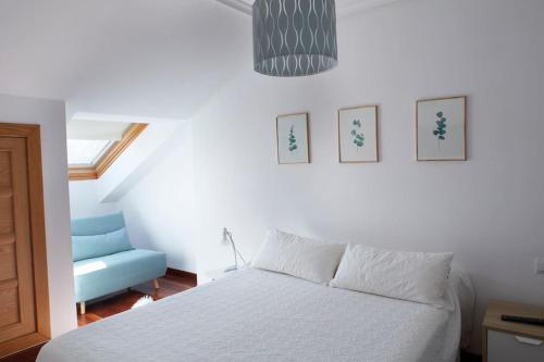 a bedroom with a white bed and a blue chair at Apartamento con terraza a un paso de la playa in Gijón