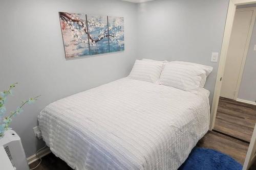 ein Schlafzimmer mit einem weißen Bett und einem Gemälde an der Wand in der Unterkunft Cheerful 2-Bedroom Apartment with Smart Home Tech. in Uniondale