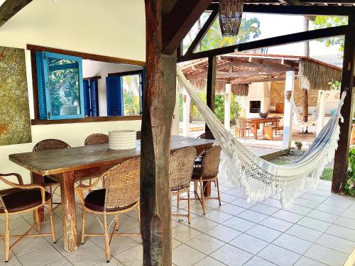 a patio with a wooden table and chairs and a hammock at Casa Bonita da Barra - 04 quartos, 170m da praia barramar in Barra de São Miguel