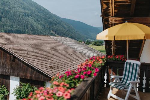a balcony with flowers and a chair and an umbrella at Residence Obermoarhof - Family Apartments with Pool & Playground in Vandoies