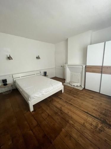 biała sypialnia z łóżkiem i drewnianą podłogą w obiekcie Gite les colombages w mieście Doudeville