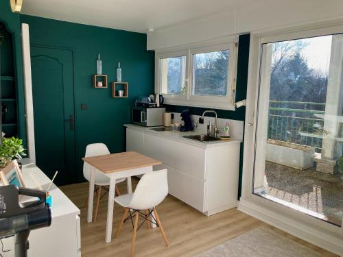cocina con paredes verdes, mesa y sillas en Appartement avec terrasse et parking gratuit accolé, en Montbéliard