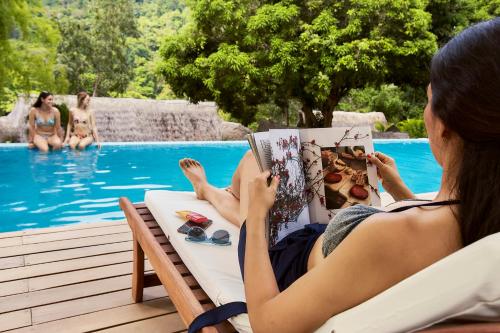 a woman sitting in a chair reading a book next to a swimming pool at Pumarinri Amazon Lodge in Tarapoto