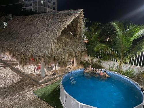 un grupo de personas en una piscina con una cabaña de paja en Cabaña los Abuelos, en Coveñas