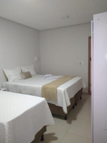 a bedroom with two beds with white sheets and a mirror at Pousada Chayenne in Piranhas