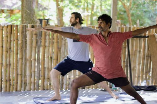 Dois homens estão a fazer ioga em frente a uma cerca de madeira. em Yoga Culture Palolem em Palolem