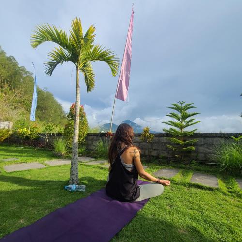 a woman sitting on a yoga mat in front of a palm tree at Volcano Lake View in Kintamani