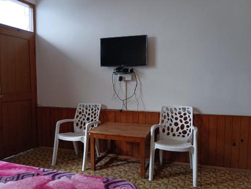 two chairs and a wooden table with a tv on a wall at ROOP MOUNTAIN HOMESTAY No Parking in Manāli