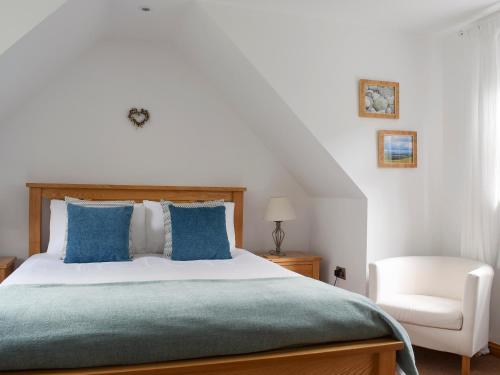 a bedroom with a bed with blue pillows and a chair at Acorn Cottage in Kippen