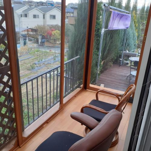 a room with two chairs on a balcony with large windows at ADD House Nara in Kanmaki
