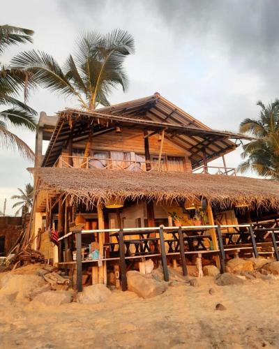 a house with a straw roof and a palm tree at Indika Beach Villa in Galle