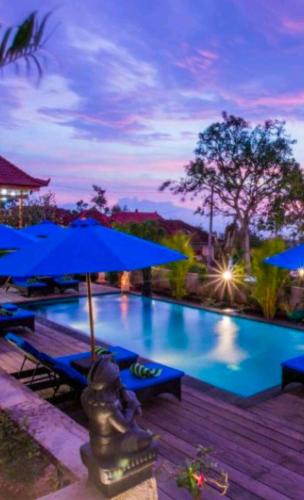 a large swimming pool with blue umbrellas and chairs at Tatak Bunut Villa Ceningan in Nusa Lembongan