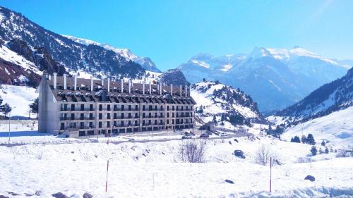 um edifício na neve com montanhas ao fundo em Apartamentos Pirineos Rent em Candanchú