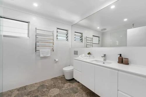 a white bathroom with a toilet and a sink at Broadbeach Bungalow - Heated Pool - Sleeps 7 in Gold Coast
