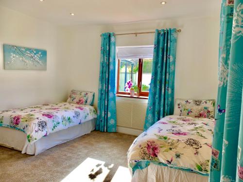 two beds in a room with blue curtains and a window at Honeyacres in Down Hatherley
