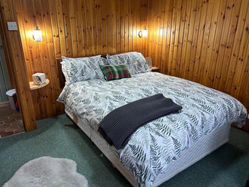 a bed in a room with a wooden wall at Craiglea Cottage, self catering highland cottage. in Fort William