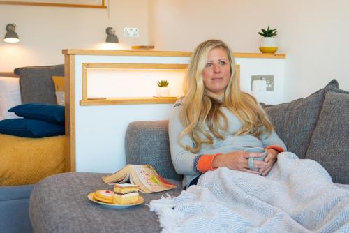 a woman sitting on a couch with a plate of food at Bonnie Barns - Adults Only Luxury Lodges with hot tubs in Luss