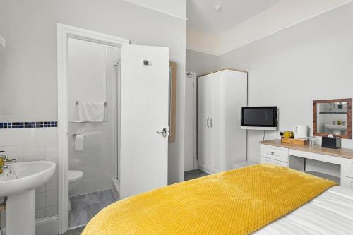 a white bathroom with a sink and a bed with a yellow blanket at South view in Torquay