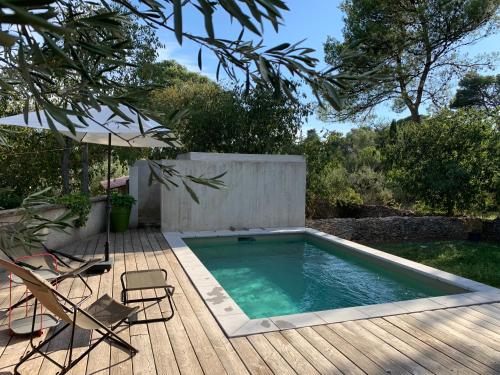 - une piscine sur une terrasse en bois avec 2 chaises et un parasol dans l'établissement Loumaset-agréable petite maison-garrigues de Nîmes, à Nîmes