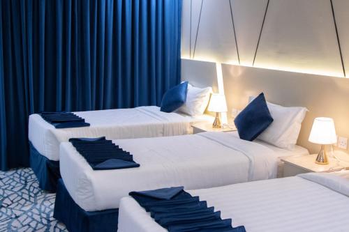 two beds in a hotel room with blue curtains at سويتس المقام in Makkah