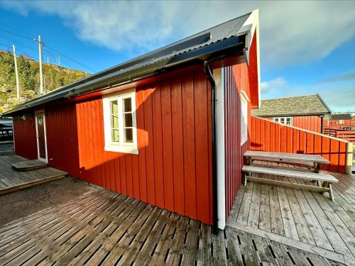 a red building with a bench on a deck at Ocean View Tind Lofoten in Moskenes