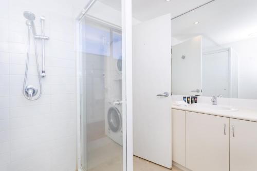 a white bathroom with a shower and a sink at Cottesloe Azura Apartment in Perth