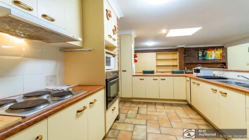a kitchen with white cabinets and a stove top oven at Banksia Gem One Street Back From Waterfront in Banksia Beach