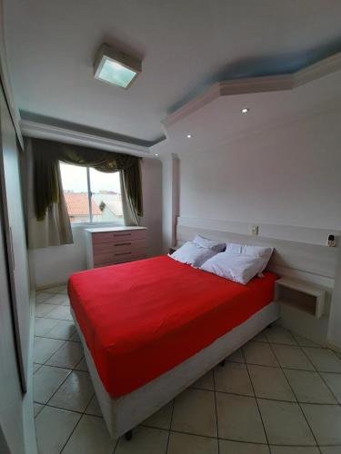 1 dormitorio con cama roja y ventana en Estrela do mar 3 dormt, en Bombinhas