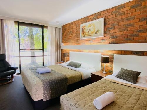 a hotel room with two beds and a brick wall at Connells Motel & Serviced Apartments in Traralgon