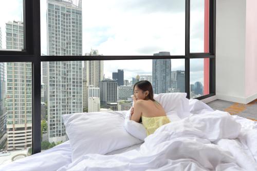 BelAire Bangkok Sukhumvit - SHA Extra Plus في بانكوك: امرأة جالسة على سرير في غرفة مع نافذة