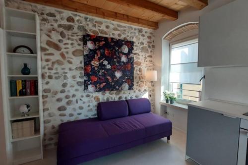 Sofá púrpura en una habitación con pared de piedra en Sui Tetti di Valeggio - Holiday Apartment, en Valeggio sul Mincio