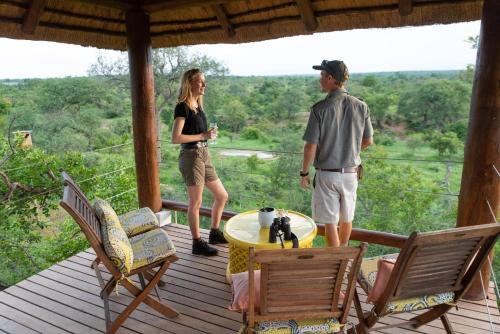 un homme et une femme debout sur le pont d'une maison dans l'établissement Sausage Tree Safari Camp, à Réserve de Balule