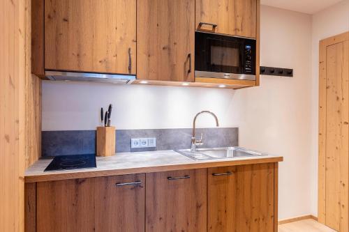 a kitchen with wooden cabinets and a sink and a microwave at Dorfresort Kitzbühel by ALPS RESORTS in Reith bei Kitzbühel