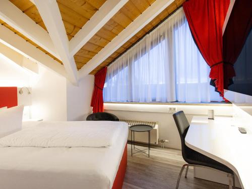 Schlafzimmer mit einem Bett, einem Schreibtisch und einem Fenster in der Unterkunft DORMERO Hotel Düsseldorf in Düsseldorf
