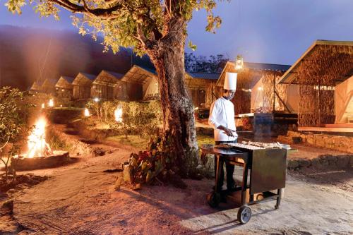 a man cooking food on a grill next to a tree at Wild Glamping Knuckles - Thema Collection in Rangala