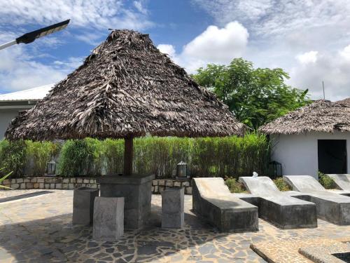 Cabaña de paja con bancos, mesa y sillas en Maison madasgascar, en Ampasikely