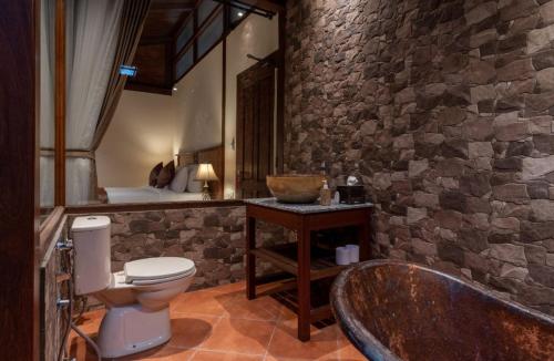 a stone bathroom with a toilet and a bath tub at DAMAI in Canggu