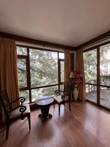 een woonkamer met een tafel, stoelen en ramen bij Villa Bliss Lake View in Nainital