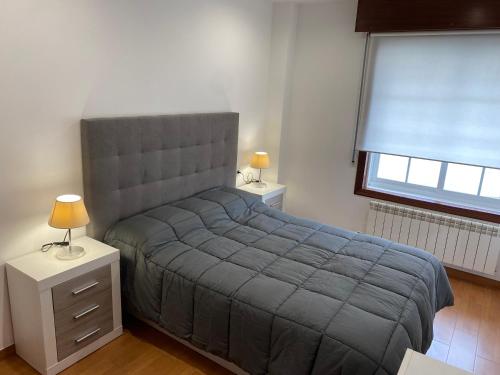 1 dormitorio con 1 cama con manta gris y ventana en SANTA MARTA PLAYA BAIONA, en Baiona