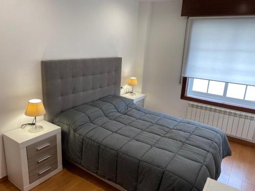 a bedroom with a bed with a gray blanket and a window at SANTA MARTA PLAYA BAIONA in Baiona