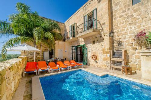 a swimming pool with orange chairs and a building at Razzett Tuta Holiday Home in Kerċem