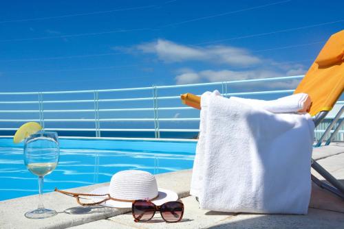 een hoed en zonnebril en een glas wijn naast een zwembad bij Sol do Lido 2 in Funchal