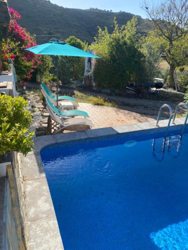 a blue swimming pool with an umbrella and two chairs at Country guest house with pool in Tavira