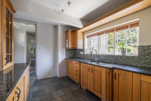 een keuken met houten kasten, een wastafel en een raam bij Putsborough Manor 3 Self Catering Cottages with Beach a short walk, dog friendly all year, On site Tennis, Play Area, Paddock, Spa baths, BBQ, Private Gardens, Superfast WIFI in Croyde